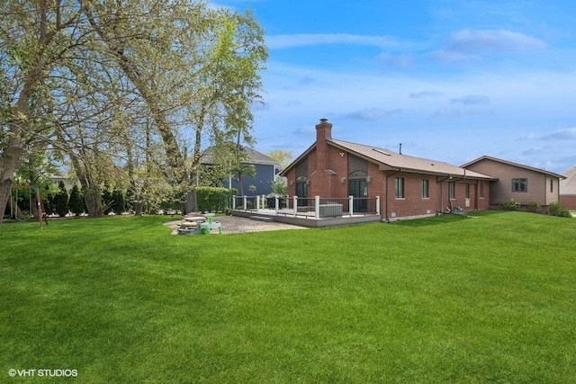 back of house with a chimney, a yard, a deck, and brick siding