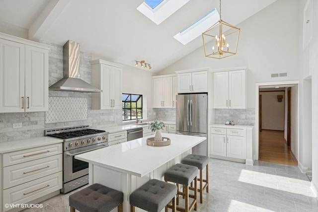 kitchen with stainless steel appliances, wall chimney range hood, a skylight, a breakfast bar, and a chandelier
