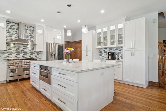 26464 N Bittersweet Trl, Mundelein, IL 60060 - kitchen featuring appliances with stainless steel finishes, wall chimney exhaust hood, tasteful backsplash, white cabinetry, and light wood-type flooring