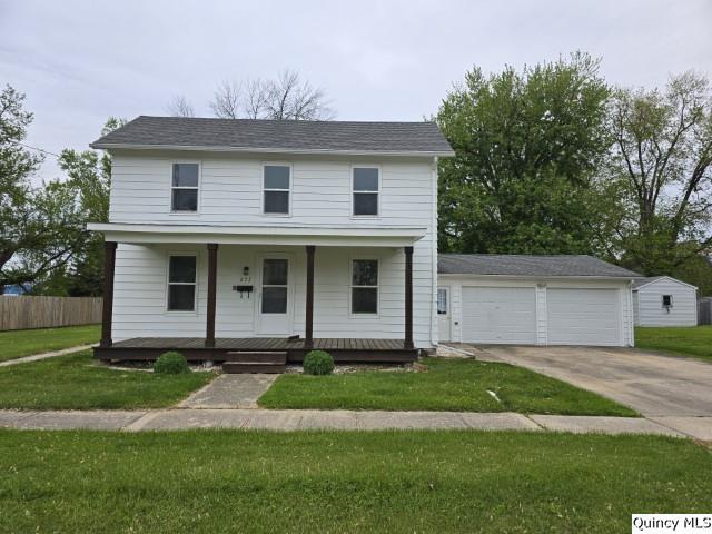 traditional home featuring a porch, a front lawn, fence, and a detached garage