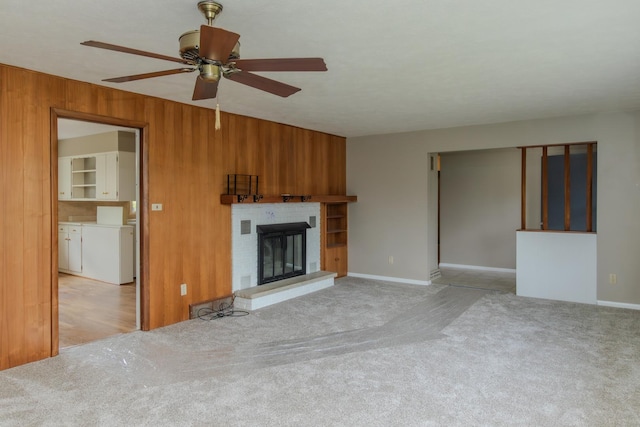 unfurnished living room with wood walls, a ceiling fan, carpet, a brick fireplace, and baseboards