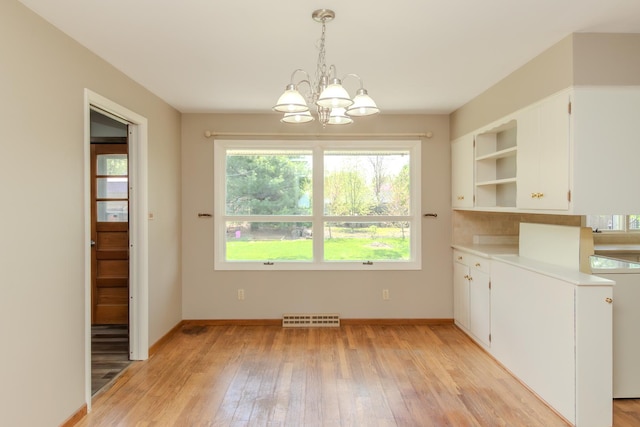 unfurnished dining area with a chandelier, light wood-style floors, and baseboards