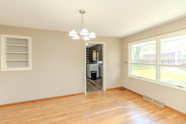 unfurnished room with washer and clothes dryer, baseboards, a chandelier, light wood-style floors, and built in shelves