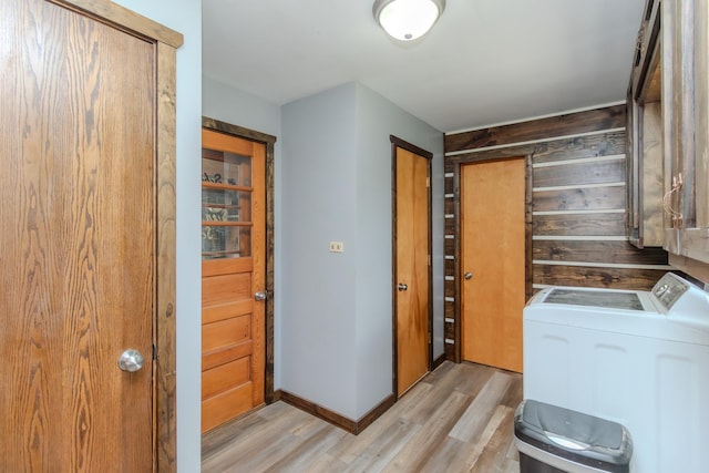 laundry area with light wood-style flooring, wood walls, washer and clothes dryer, and baseboards