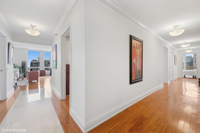 hallway featuring light wood finished floors, crown molding, and baseboards