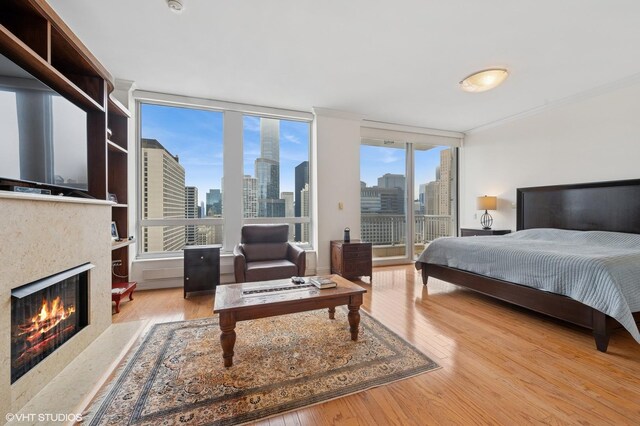 bedroom featuring a high end fireplace, a city view, access to outside, and wood finished floors