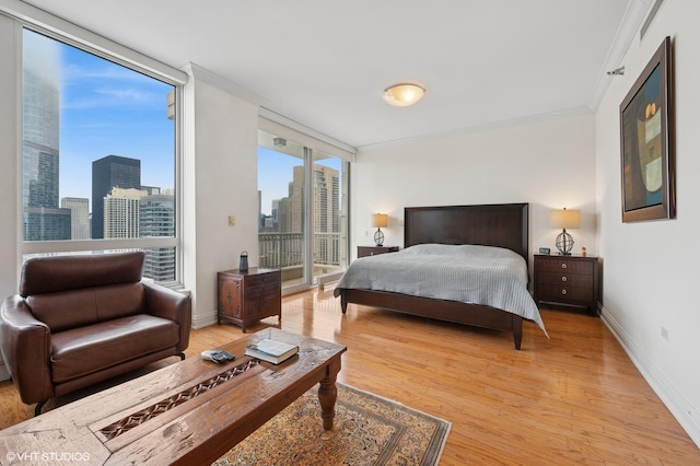 bedroom with baseboards, a view of city, access to outside, crown molding, and light wood-type flooring