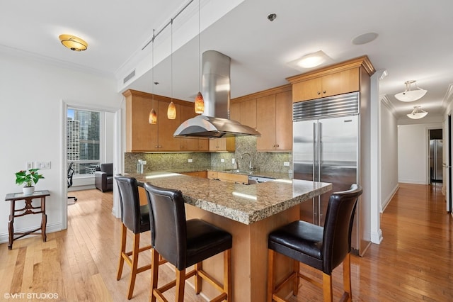 kitchen with island exhaust hood, built in fridge, a sink, visible vents, and tasteful backsplash