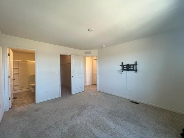 unfurnished bedroom with baseboards, visible vents, light colored carpet, and a walk in closet