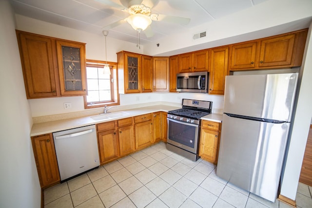 kitchen with appliances with stainless steel finishes, a sink, brown cabinetry, light countertops, and a ceiling fan
