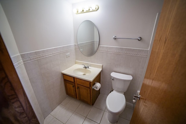 half bathroom featuring toilet, wainscoting, vanity, tile walls, and tile patterned flooring
