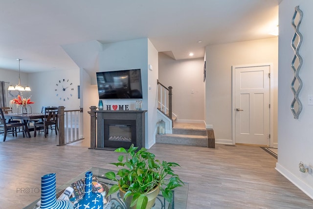 living area featuring wood finished floors, a notable chandelier, stairway, baseboards, and a glass covered fireplace