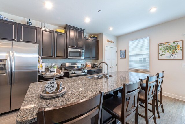kitchen featuring light wood-style flooring, light stone counters, a sink, a kitchen breakfast bar, and appliances with stainless steel finishes