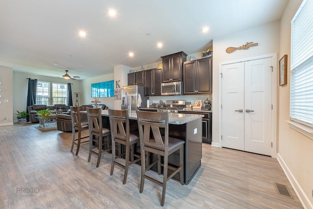 kitchen featuring a kitchen breakfast bar, a kitchen island with sink, visible vents, dark brown cabinetry, and appliances with stainless steel finishes