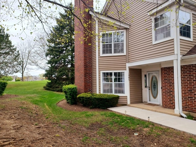 view of front of home with brick siding, a front lawn, and a chimney