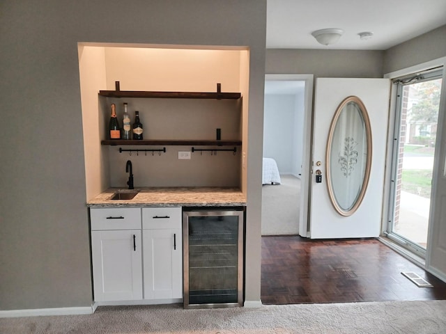 foyer with wine cooler, bar with sink, baseboards, and dark colored carpet