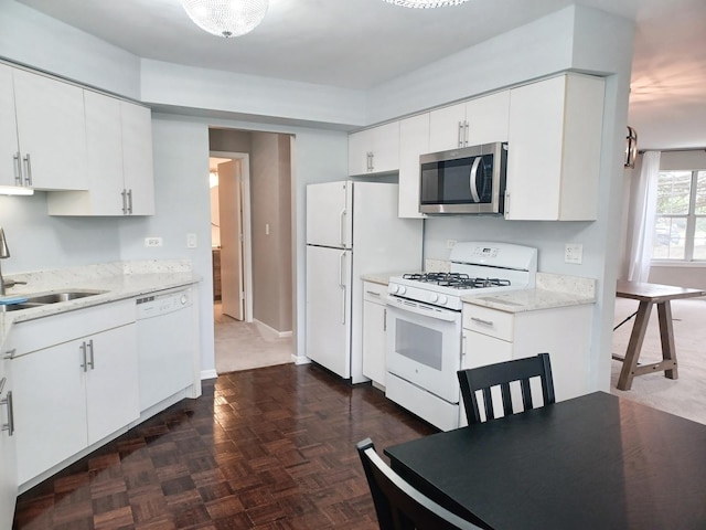 kitchen with white appliances, a sink, white cabinetry, light stone countertops, and baseboards