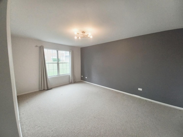 unfurnished room featuring light carpet, a chandelier, and baseboards