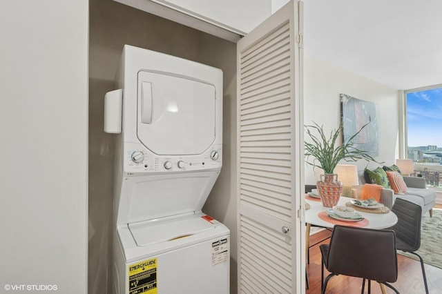 clothes washing area featuring stacked washer / drying machine and wood finished floors