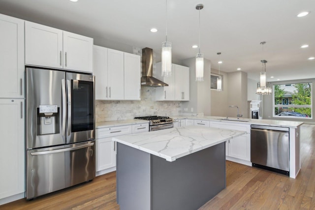 kitchen with stainless steel appliances, wall chimney exhaust hood, a sink, a peninsula, and wood finished floors