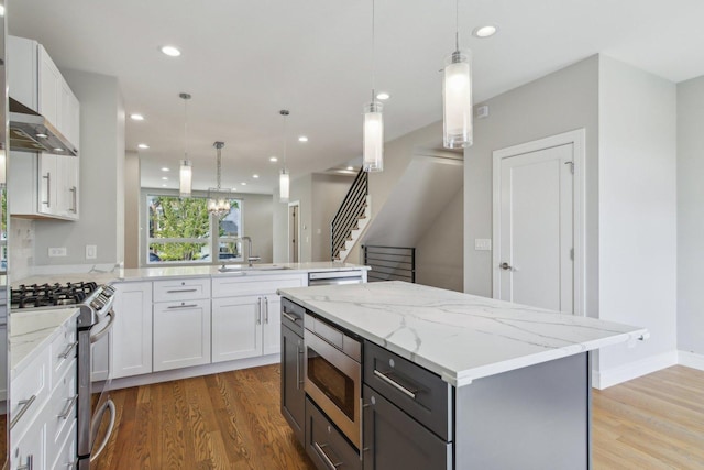 kitchen with appliances with stainless steel finishes, a sink, a peninsula, light wood-type flooring, and recessed lighting