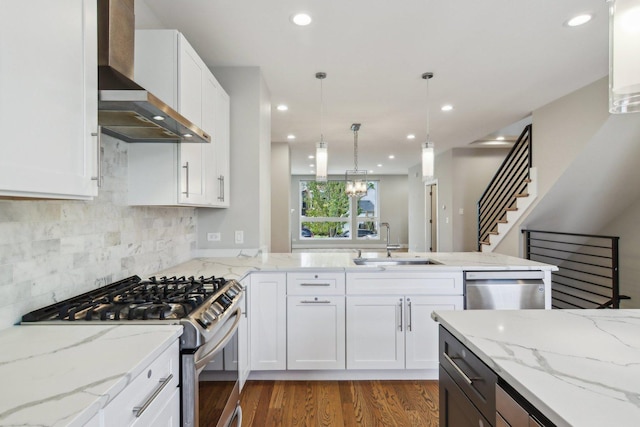 kitchen featuring appliances with stainless steel finishes, wall chimney range hood, a sink, a peninsula, and white cabinets