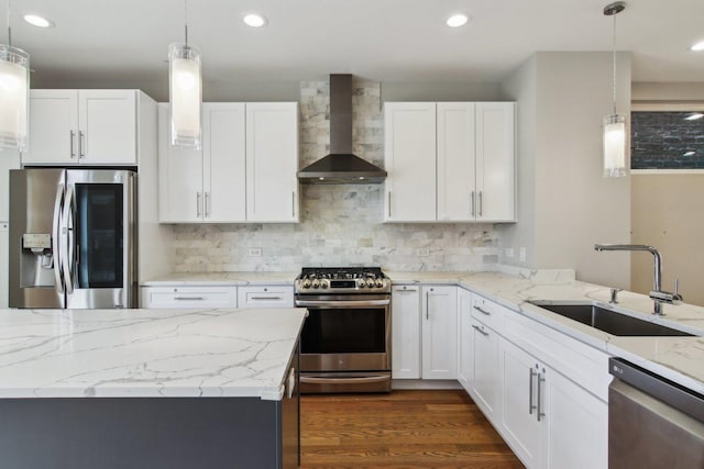 kitchen with stainless steel appliances, wall chimney exhaust hood, a sink, white cabinets, and pendant lighting