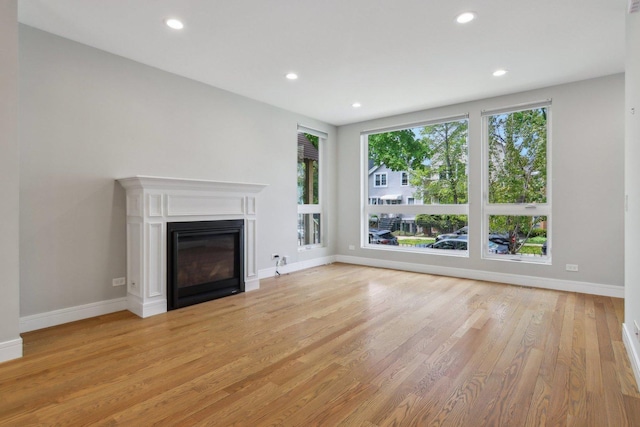 unfurnished living room featuring a glass covered fireplace, light wood-style floors, recessed lighting, and baseboards