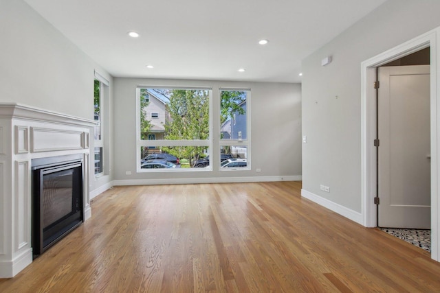 unfurnished living room featuring light wood-style flooring, a glass covered fireplace, baseboards, and recessed lighting