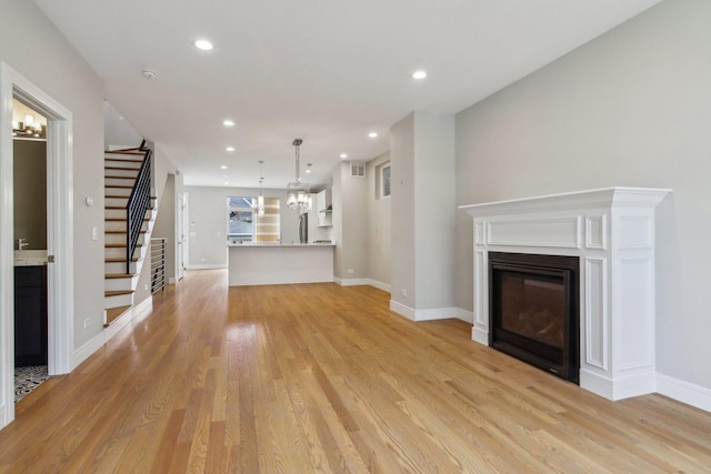 unfurnished living room with stairway, light wood-type flooring, a glass covered fireplace, recessed lighting, and a chandelier