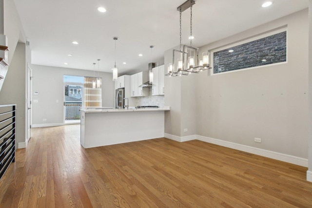 kitchen with freestanding refrigerator, wall chimney range hood, white cabinetry, light countertops, and light wood-type flooring