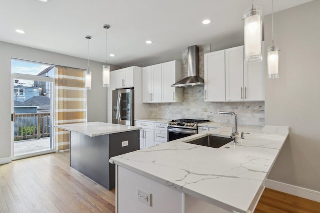 kitchen featuring wall chimney exhaust hood, appliances with stainless steel finishes, a sink, backsplash, and light stone counters