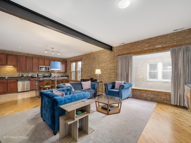 living area featuring light wood-type flooring, visible vents, and brick wall