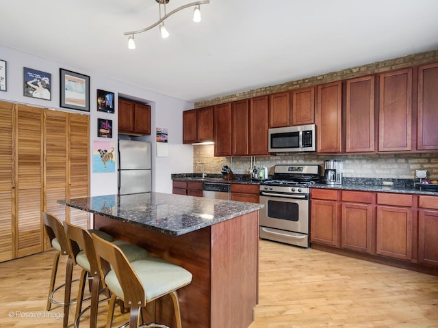 kitchen featuring a kitchen island, stainless steel appliances, light wood-style flooring, and backsplash