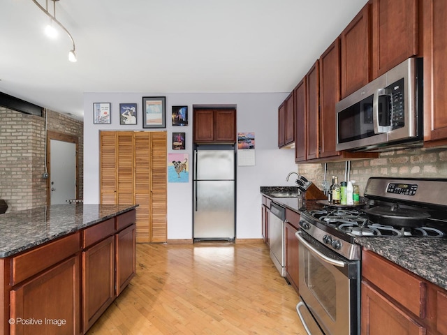 kitchen featuring a sink, dark stone counters, light wood-type flooring, backsplash, and appliances with stainless steel finishes