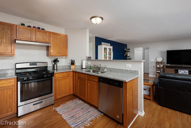 kitchen with stainless steel appliances, a sink, under cabinet range hood, open floor plan, and a peninsula