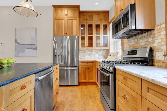 kitchen featuring glass insert cabinets, stainless steel appliances, light wood-type flooring, decorative light fixtures, and decorative backsplash