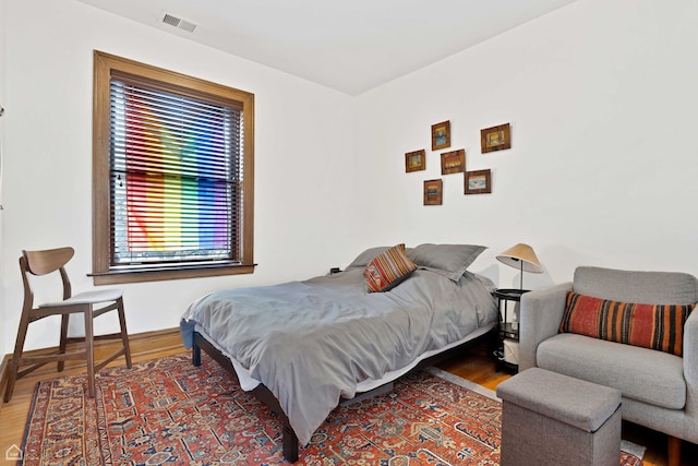 bedroom with baseboards, visible vents, and wood finished floors