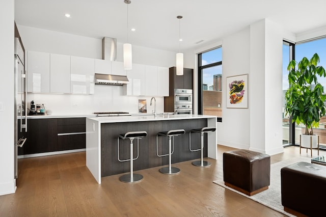 kitchen featuring wood finished floors, under cabinet range hood, white cabinetry, light countertops, and modern cabinets