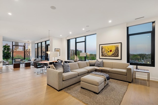 living room with a wealth of natural light, expansive windows, visible vents, and light wood-style floors
