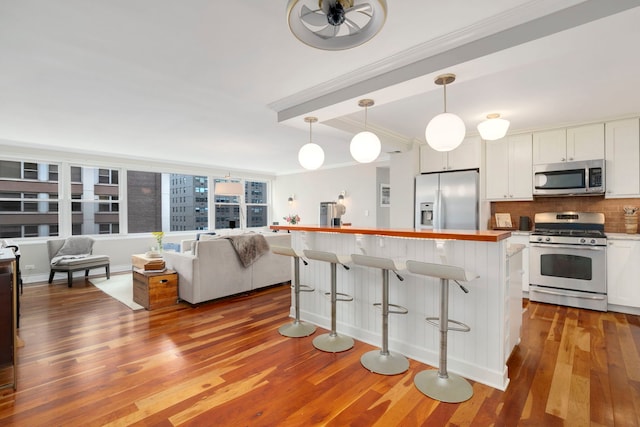 kitchen featuring stainless steel appliances, wood-type flooring, ornamental molding, open floor plan, and white cabinets