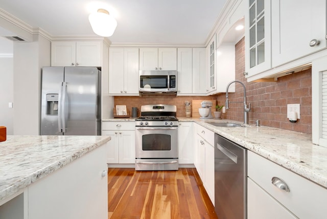 kitchen featuring appliances with stainless steel finishes, a sink, light wood-style floors, white cabinets, and tasteful backsplash