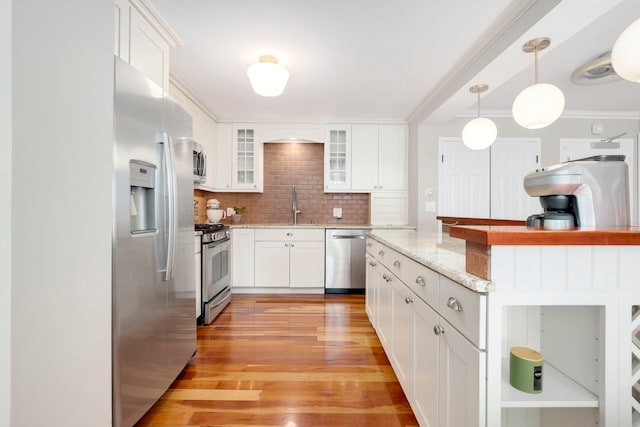 kitchen featuring appliances with stainless steel finishes, a sink, tasteful backsplash, light wood-type flooring, and white cabinets