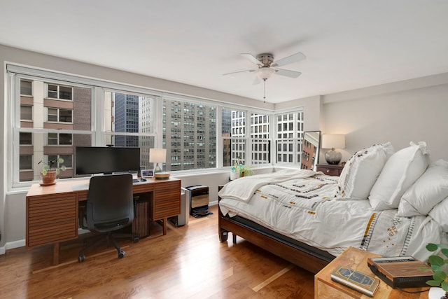 bedroom featuring wood finished floors, baseboards, a ceiling fan, and a desk