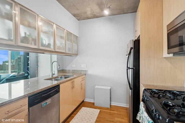kitchen with black appliances, a sink, light wood-style flooring, light stone counters, and light brown cabinets