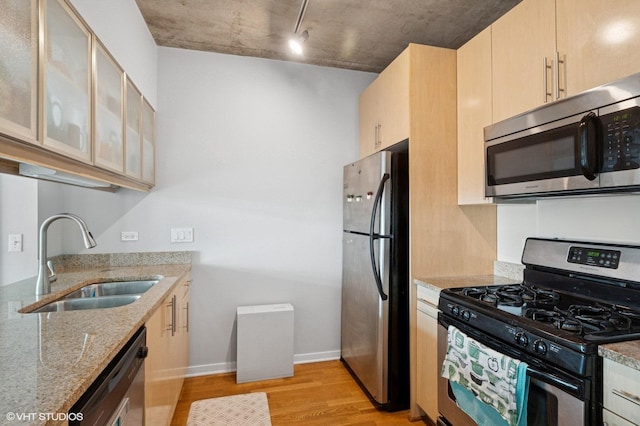kitchen with stainless steel appliances, a sink, light wood-style floors, light stone counters, and glass insert cabinets
