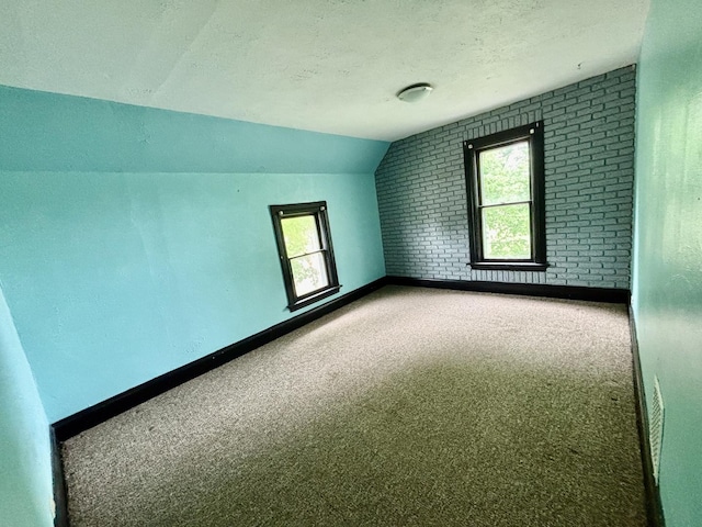 empty room featuring carpet flooring, brick wall, a textured ceiling, baseboards, and vaulted ceiling