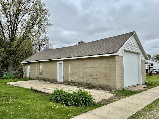 back of property with a yard, an outbuilding, a patio, concrete block siding, and a shingled roof