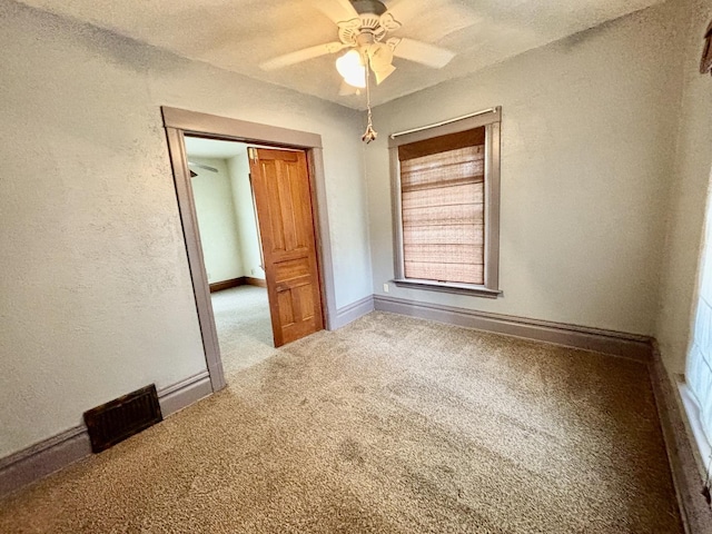 spare room with carpet, visible vents, a textured wall, a ceiling fan, and baseboards