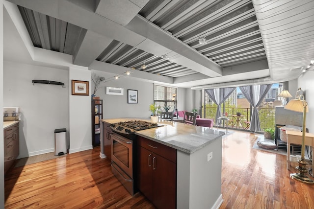 kitchen with light stone counters, stainless steel gas range oven, open floor plan, and light wood-style flooring